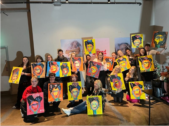 Beyond the Mirror event where attendees are holding up completed paintings of Frida Kahlo