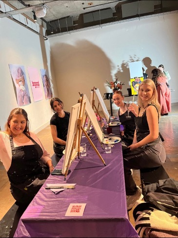 Women smiling whilst painting Frida Kahlo and drinking wine