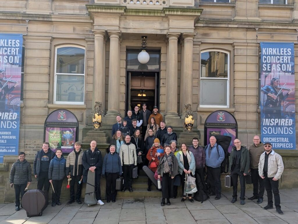 A photo of Crookes Brass Band members stood on the steps outside of Huddersfield Town Hall.