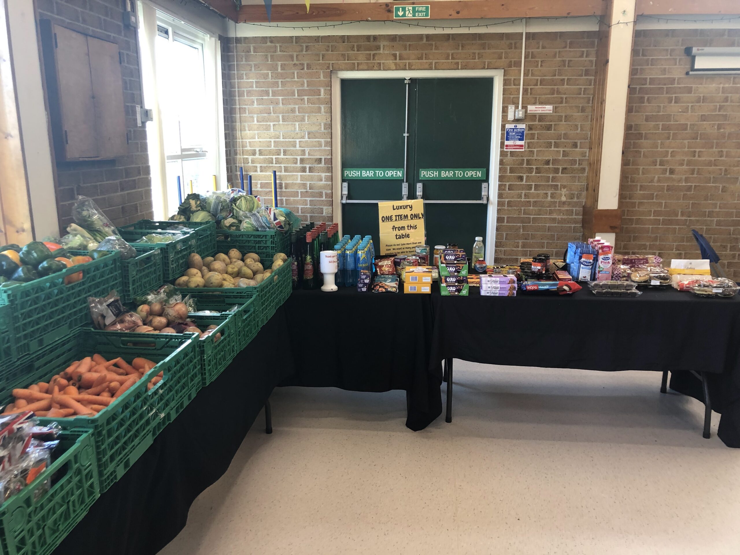 Tables in a food bank stocked with fruit, vegetables and luxury items