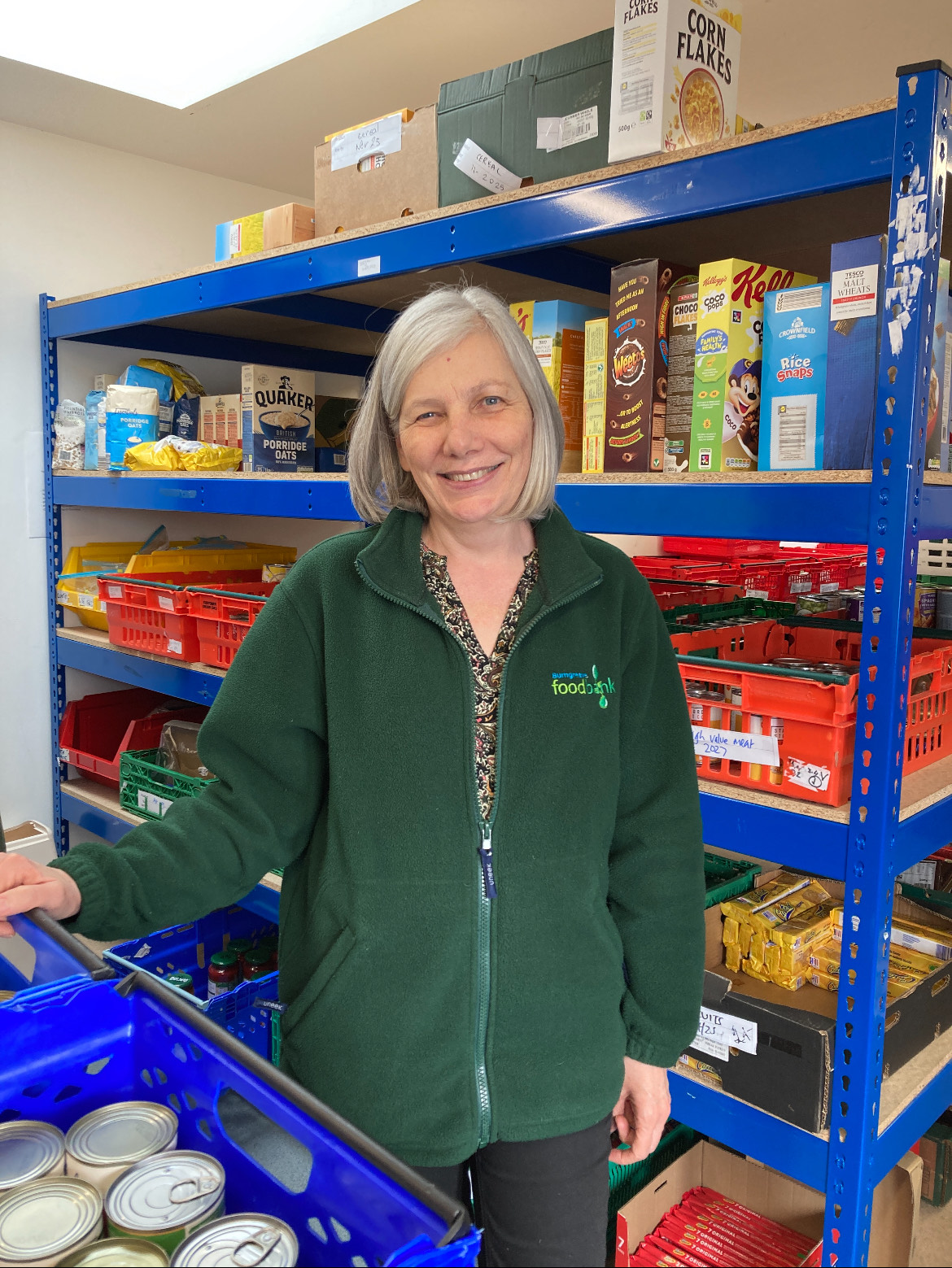 An image of a female standing in front of shelves stacked with food at the food bank.