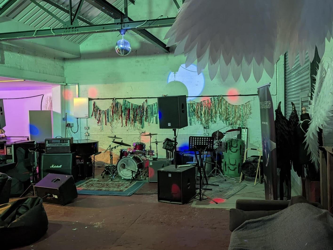A music room with green lighting, a disco ball and colourful bunting with a range of equipment and instruments, such as a drum kit, in the centre.
