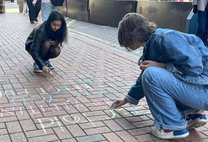 Two people writing with chalk on the pavement