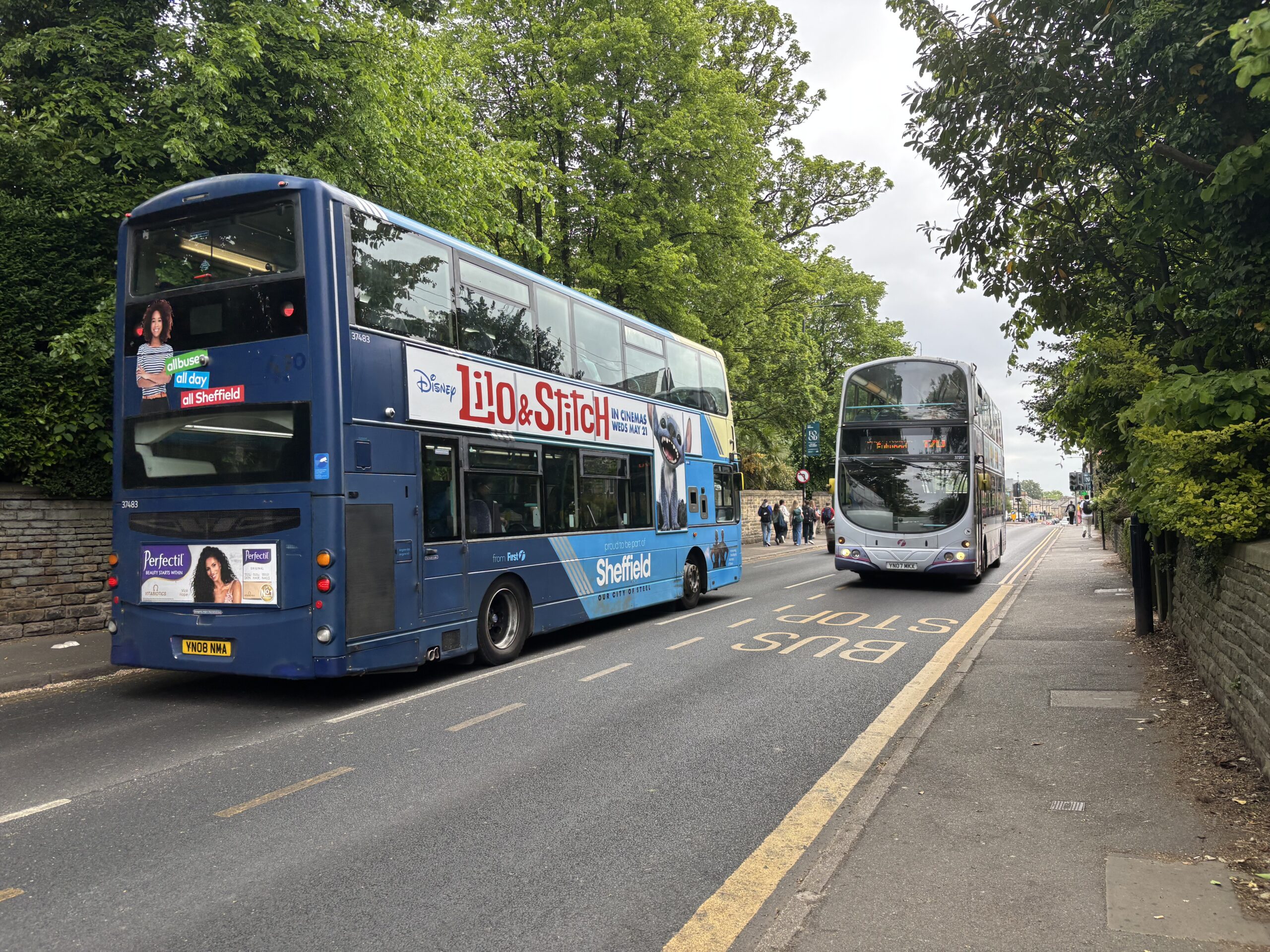 Two Sheffield 120 buses passing each other on the road. One bus is approaching a bus stop