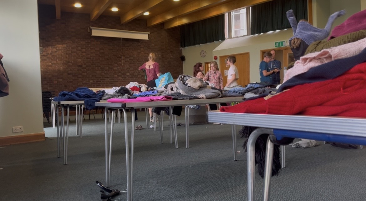 a photo of a room with tables set out for clothes to go on, people are in the room trying on the clothes