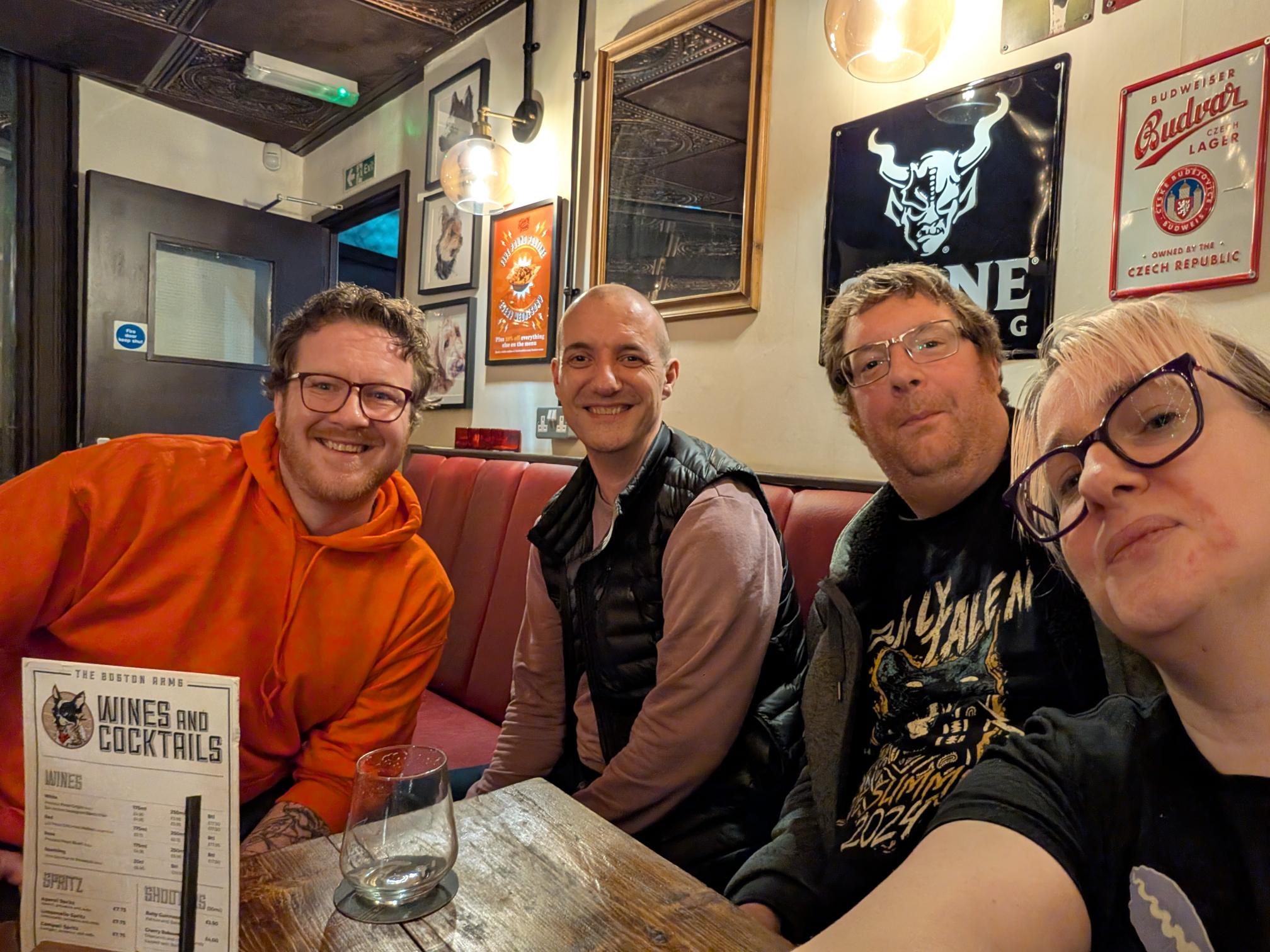 1000019145 three men and a woman sat in a pub setting, the man hosting is wearing a bright orange hoodie