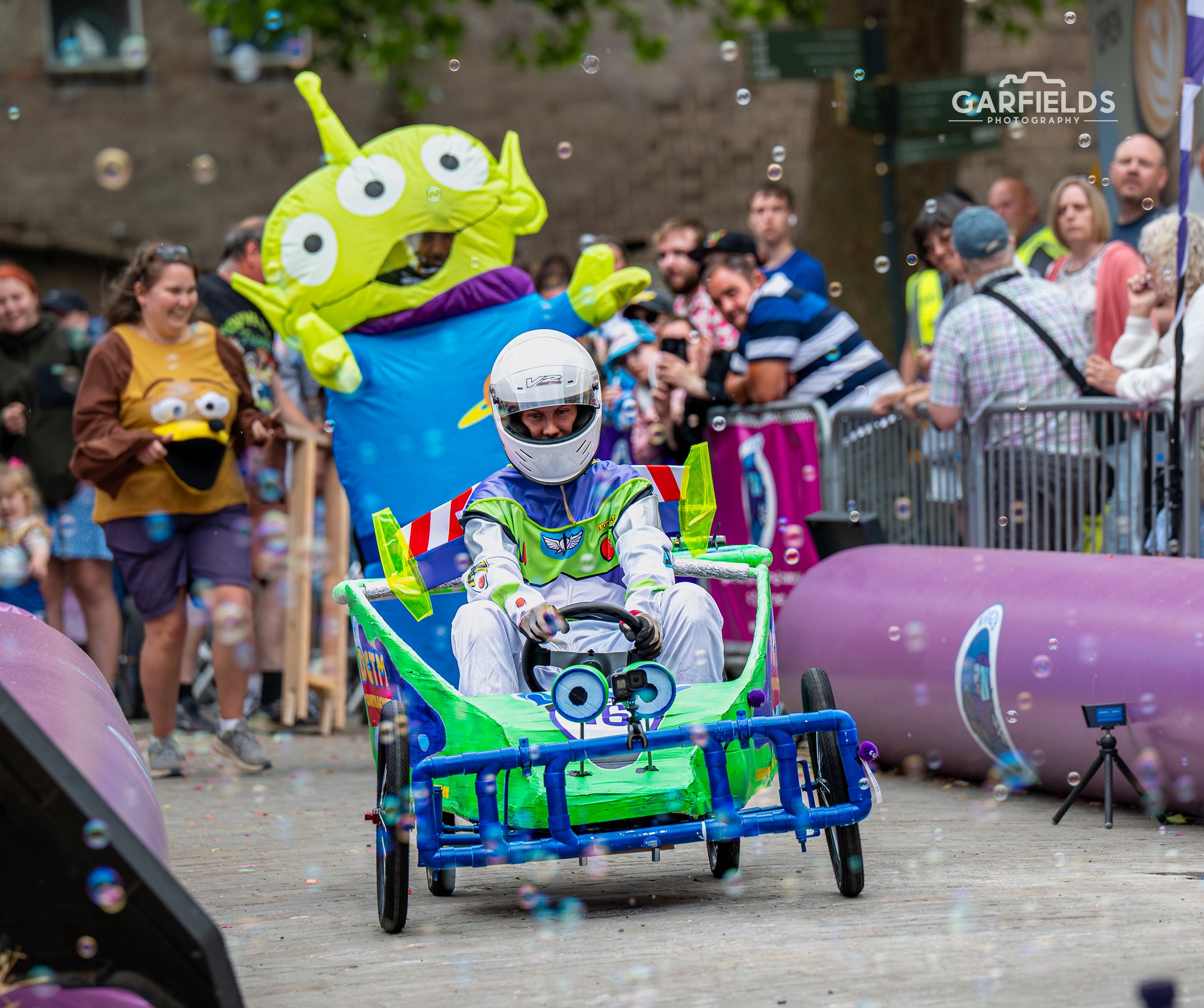 Cart in Buzz Lightyear style with racer dressed as Buzz. Three eyed Toy Story alien following behind